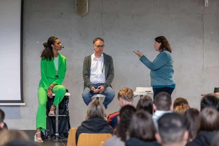 Lijana Kaggwa nimmt an einer Podiumssituation in einer Schulveranstaltung vor Publikum teil.