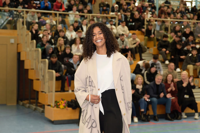 Portraet von Lijana Kaggwa in rosa Kleid vor dekorativer Kulisse fuer Medien, Oeffentlichkeit und Persoenlichkeitsprofil.