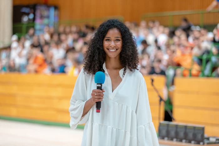 Lijana Kaggwa mit Mikrofon bei einer Schulveranstaltung vor großem Publikum